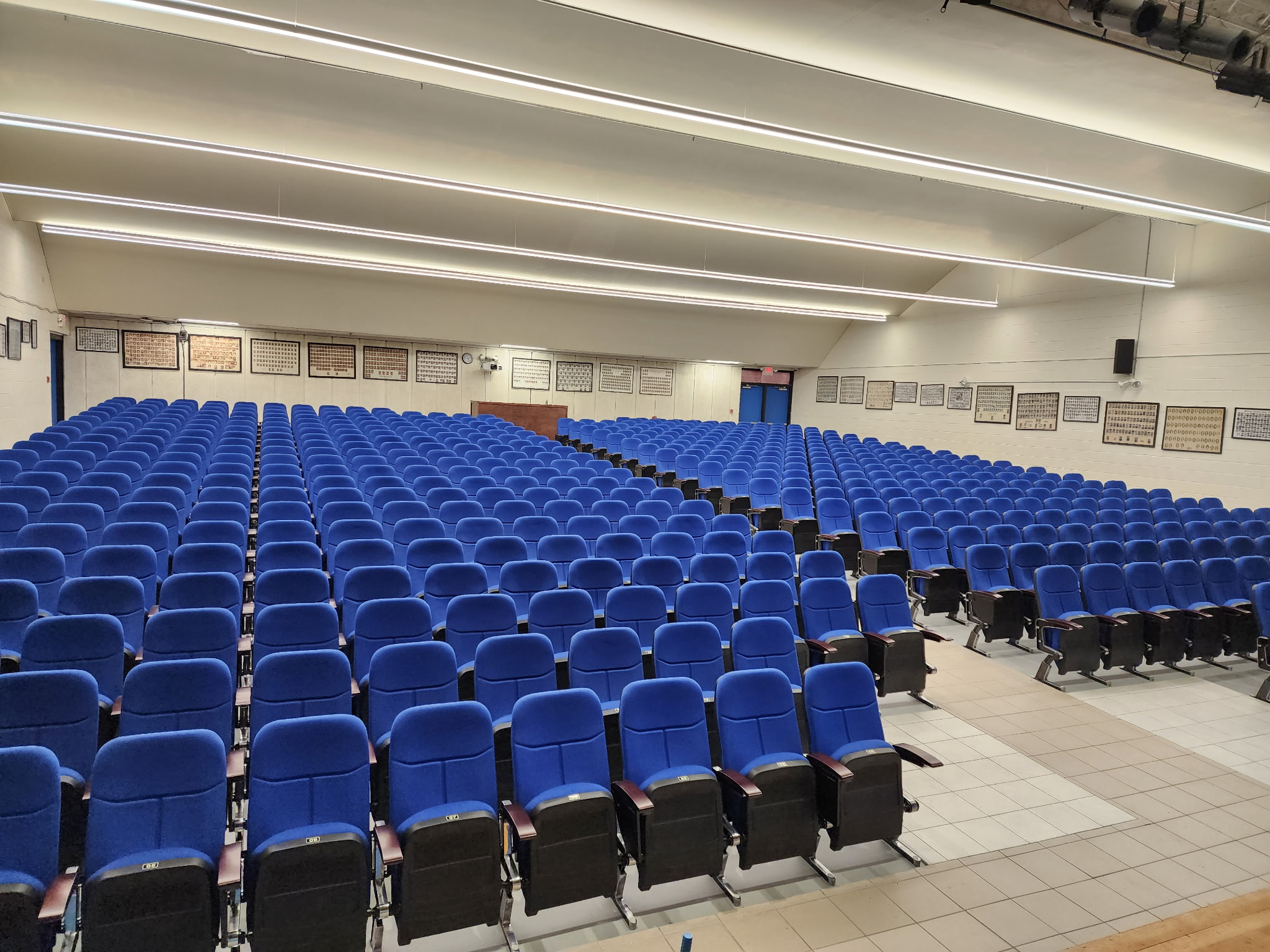 Auditorium with rows of royal-blue upholstered fixed seats, wood-tone armrests and wide aisles