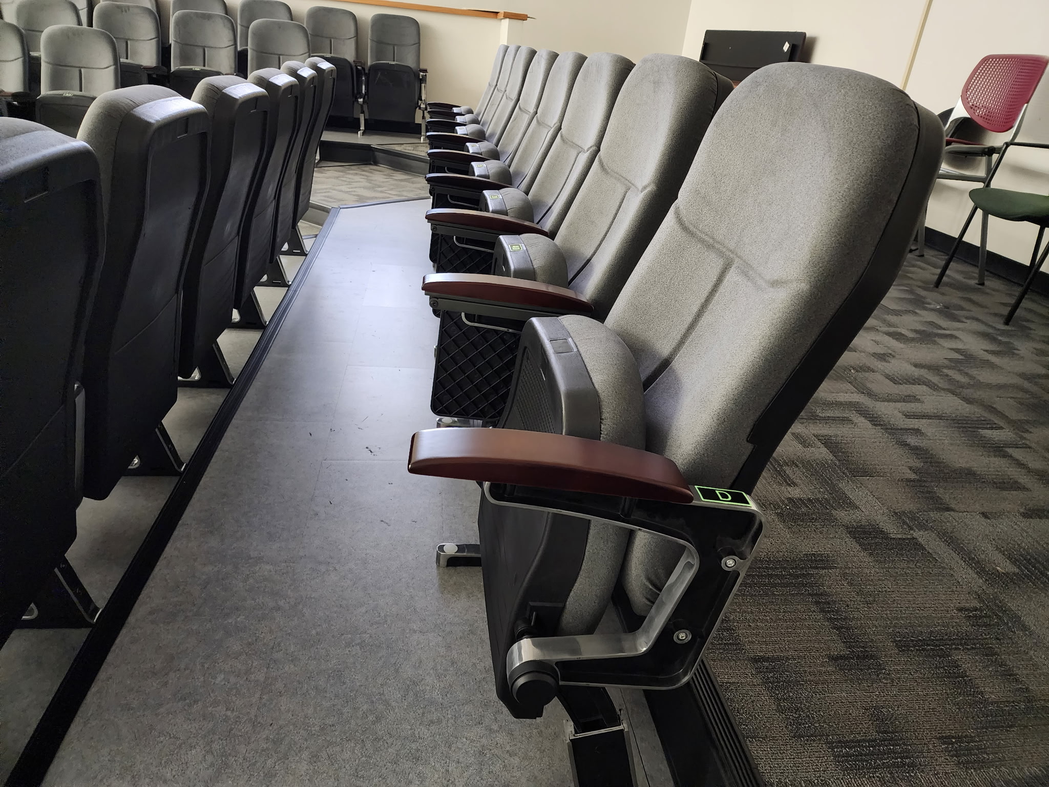 Close-up of gray upholstered fixed chairs with wood-tone armrests and folding seats