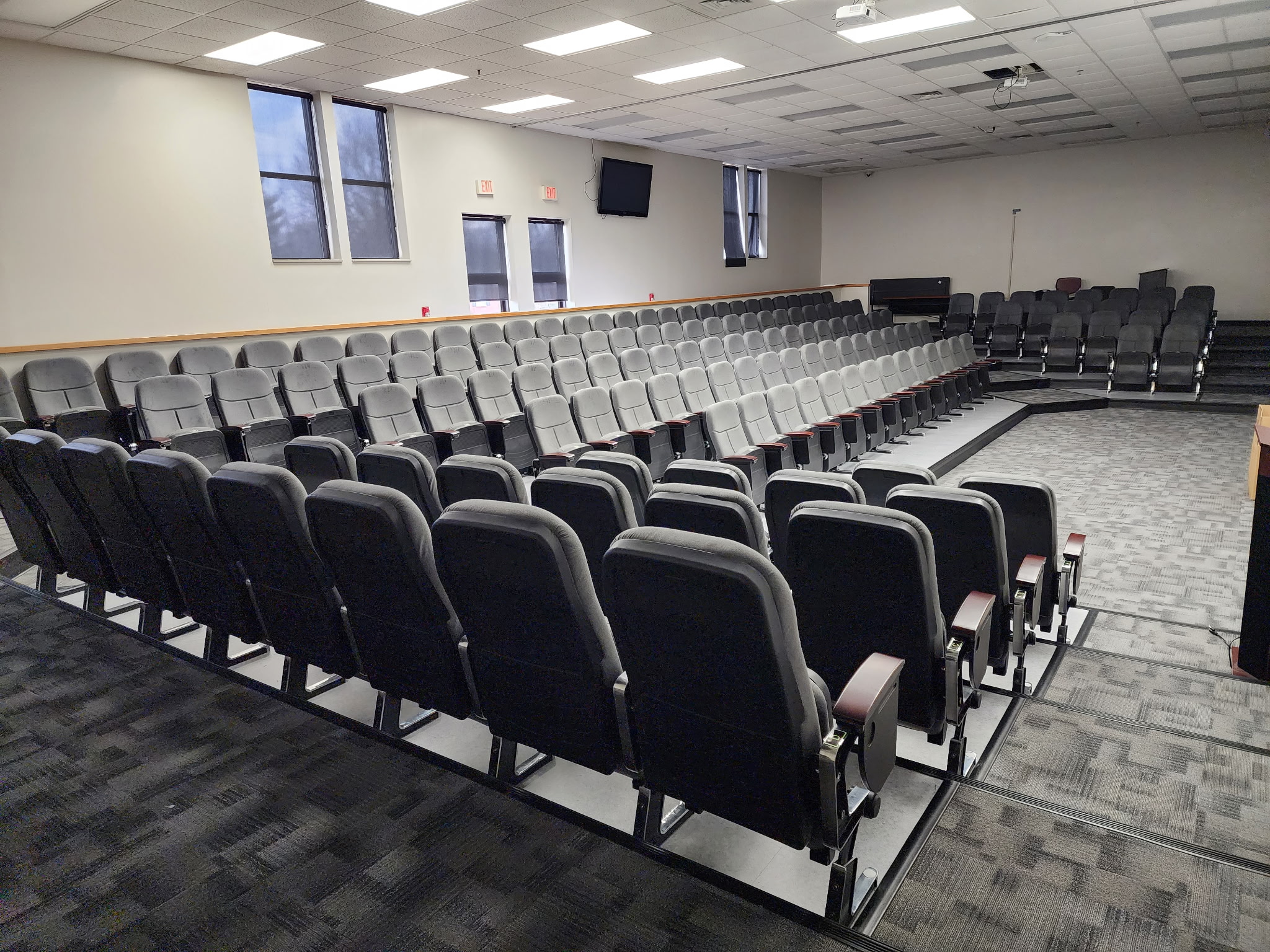 Full auditorium layout with gray upholstered fixed chairs, stepped rows and open aisles